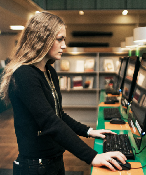 Kvinna som anv&auml;nder en dator st&aring;ende p&aring; ett skrivbord.